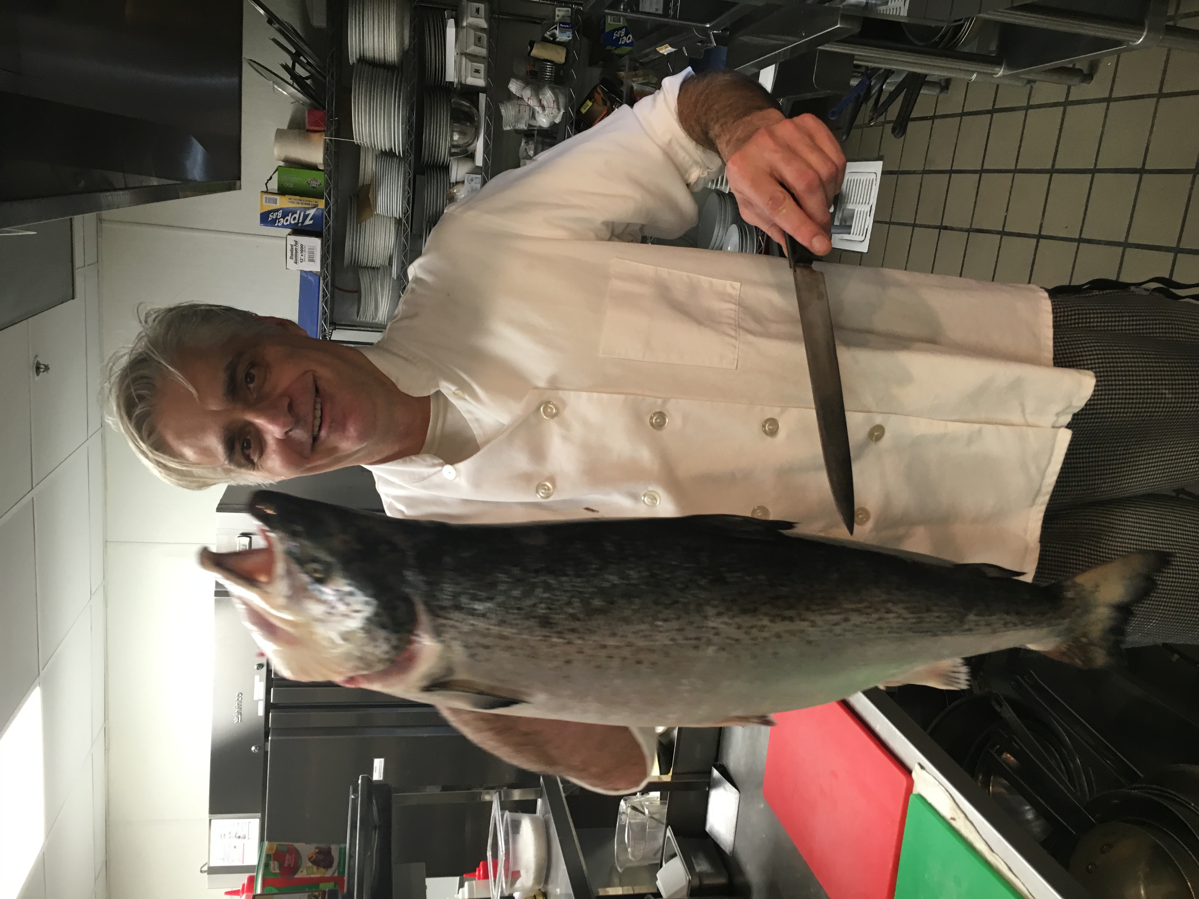 Chef David Giani holding a whole fresh salmon in a professional kitchen