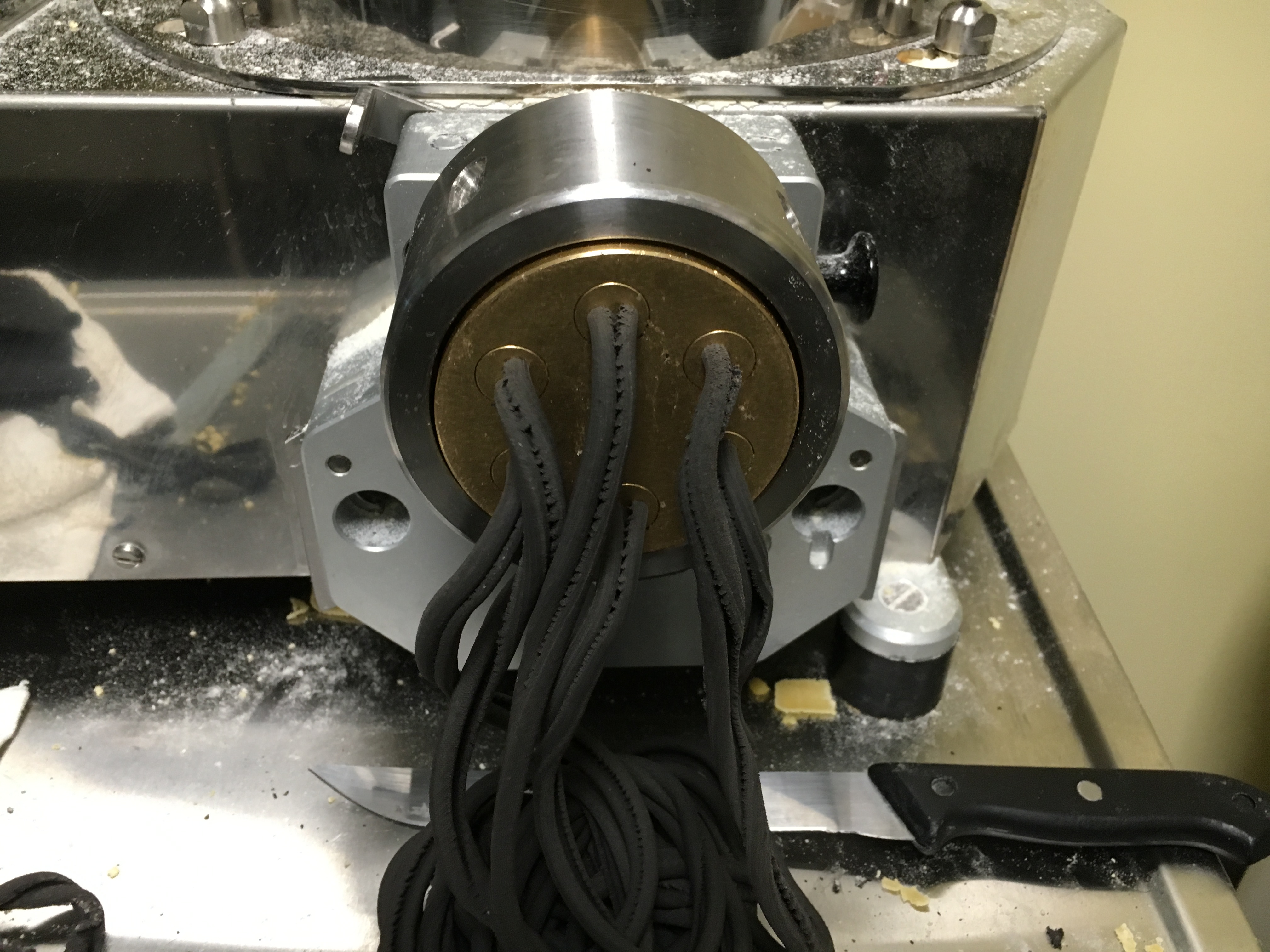 Squid ink pasta dough coming out of a modern pasta extruder die