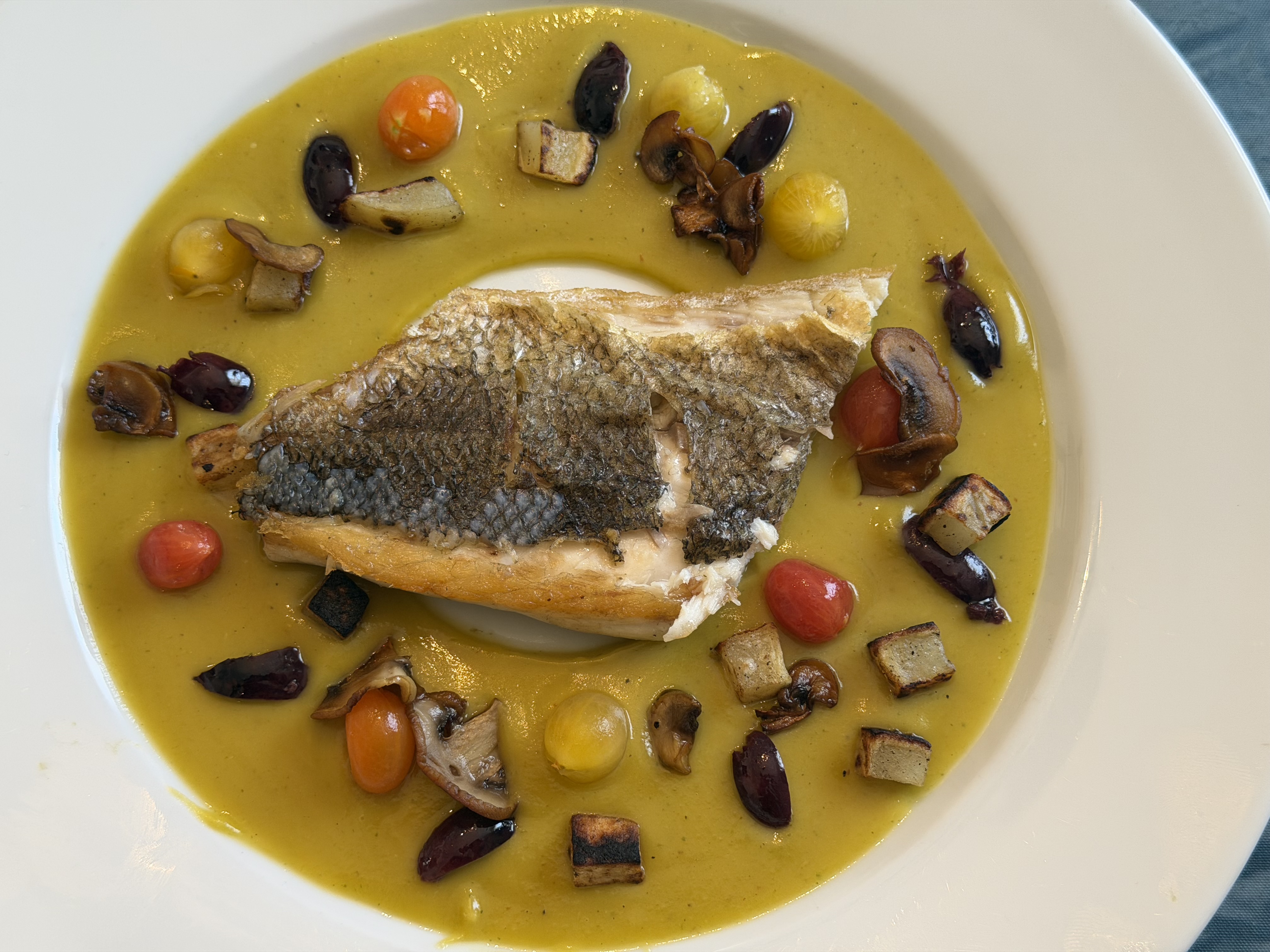Crispy branzino fillet with zucchini confiture, mushrooms, potatoes, olives, and Campari tomatoes
