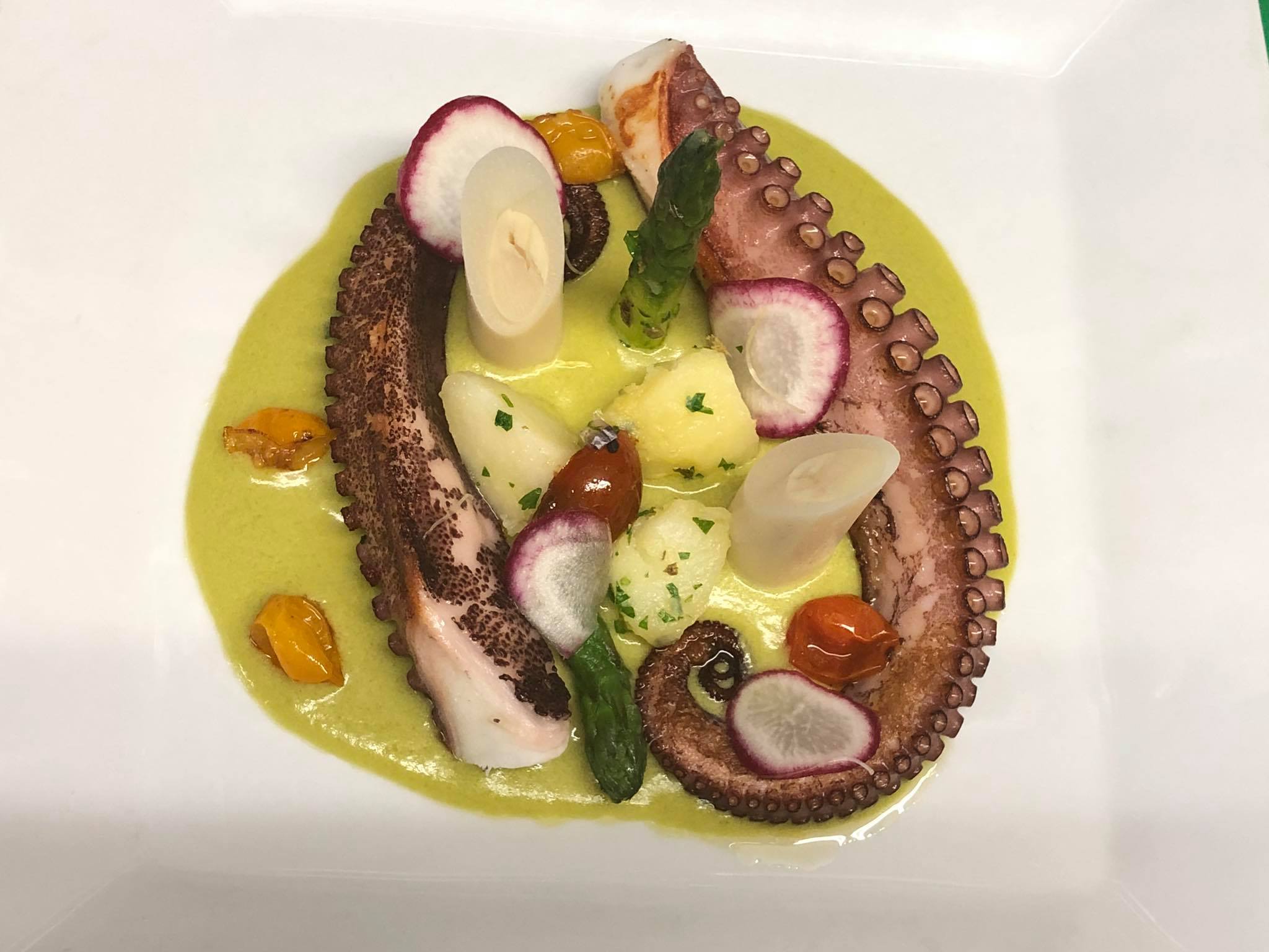 Spanish octopus plated with seasonal vegetables and asparagus emulsion